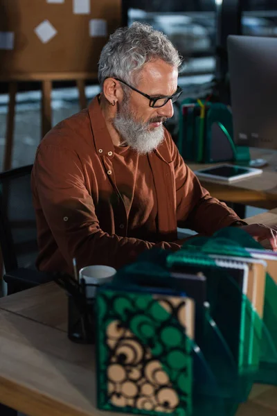 Mature businessman in eyeglasses working near notebooks and coffee in office — Stock Photo