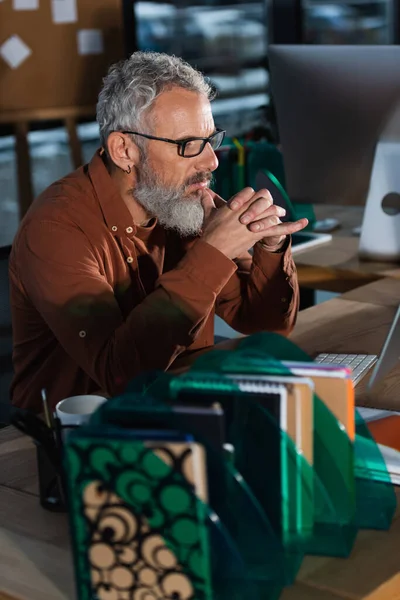 Homme d'affaires mature concentré regardant l'écran d'ordinateur près des ordinateurs portables dans le bureau en soirée — Photo de stock