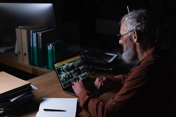 Maduro hombre de negocios que trabaja en el ordenador portátil cerca del cuaderno en blanco por la noche en la oficina — Stock Photo