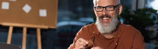 Happy bearded businessman in eyeglasses holding bitcoin and looking at camera, banner — Stock Photo