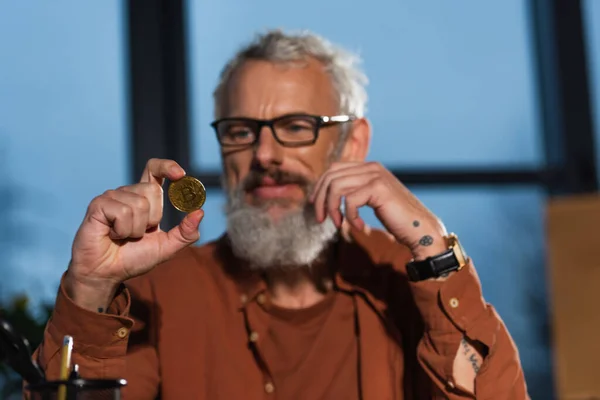 KYIV, UKRAINE - NOVEMBER 17, 2022: positive bearded businessman holding golden bitcoin on blurred background — Stock Photo