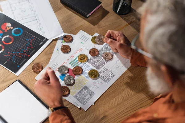 KYIV, UKRAINE - NOVEMBER 17, 2022: top view of middle aged businessman near bitcoins and documents with charts on desk in office — Stock Photo