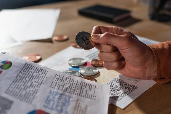 KYIV, UCRAINA - 17 NOVEMBRE 2022: bitcoin d'argento in mano a un uomo d'affari ritagliato vicino a carte sfocate con grafici — Foto stock