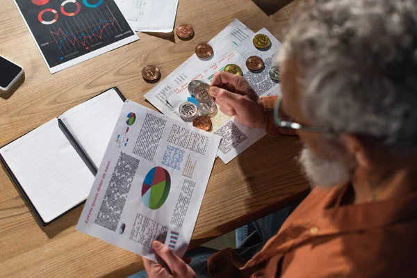 KYIV, UKRAINE - NOVEMBER 17, 2022: top view of manager holding bitcoin and infographics near notebook in office — Stock Photo
