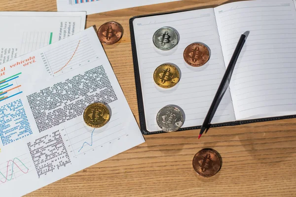 KYIV, UKRAINE - NOVEMBER 17, 2022: top view of bitcoin on empty notbook near pen and documents on office desk — стокове фото