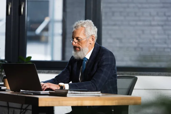 Grey haired mature man in formal wear working on laptop in office — Stock Photo