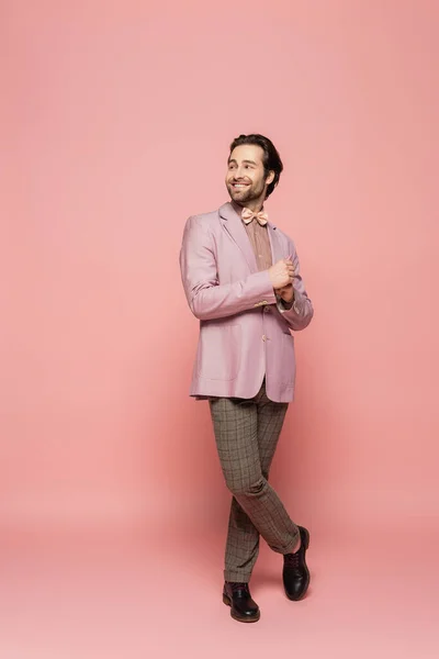 Full length of cheerful and stylish host of event looking away on pink background — Stock Photo