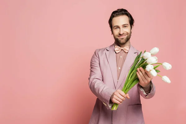 Anfitrión barbudo de evento con tulipanes blancos y mirando a la cámara sobre fondo rosa - foto de stock