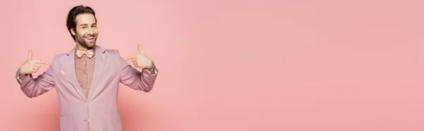Positive host of event pointing with fingers and looking at camera on pink background, banner — Stock Photo