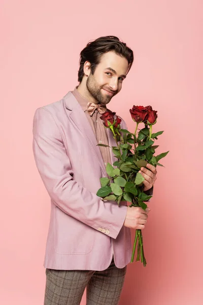 Positive host of event in jacket and bow tie holding roses on pink background — Stock Photo