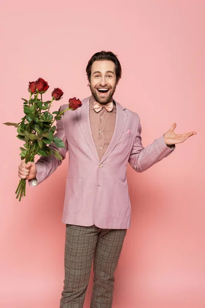 Excited host of event holding red flowers on pink background — Stock Photo