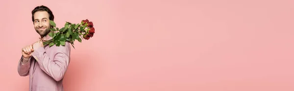 Lächelnde brünette Moderatorin mit Rosen und isoliertem Blick auf rosa Banner — Stockfoto