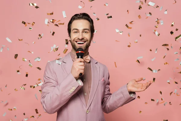 Позитивный ведущий мероприятия проведение микрофона под падение конфетти на розовый фон — стоковое фото