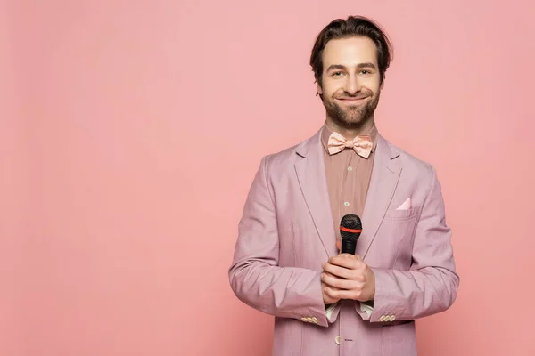 Jeune hôte de l'événement tenant le microphone et regardant la caméra isolée sur rose — Photo de stock