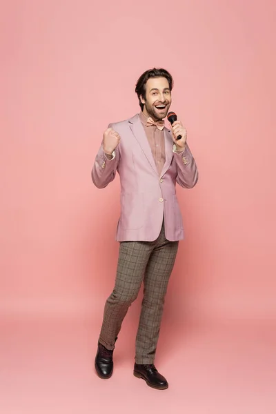 Full length of trendy host of event showing yes gesture and holding microphone on pink background — Stock Photo