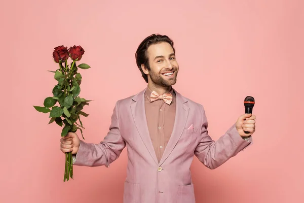 Stylish host of event in jacket and bow tie holding microphone and flowers on pink background — Stock Photo