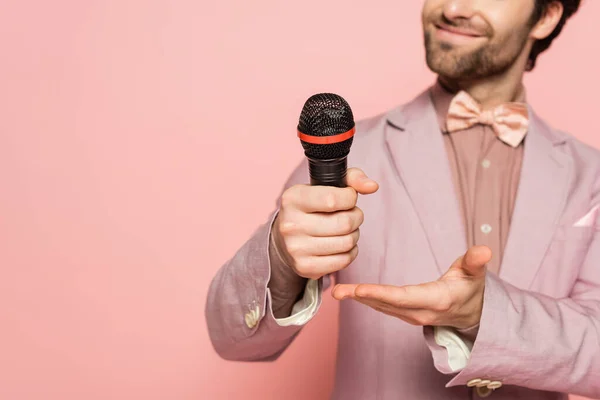 Vue recadrée de l'hôte flou de l'événement pointant vers le microphone isolé sur rose — Photo de stock