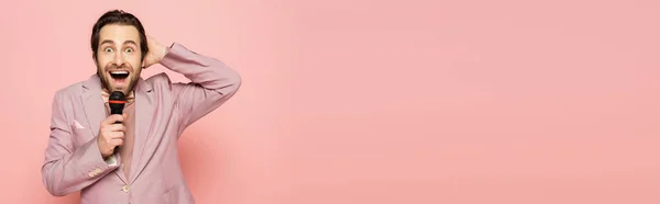 Incroyable hôte d'événement tenant microphone et regardant la caméra isolée sur rose, bannière — Photo de stock