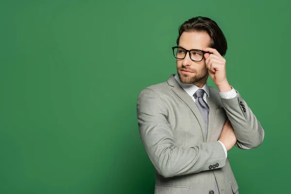Young newscaster in suit touching eyeglasses on green background — Stock Photo