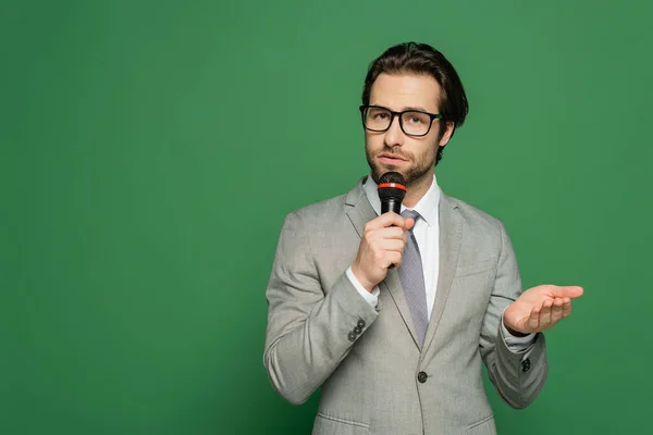Brünette Nachrichtensprecherin mit Brille spricht am Mikrofon auf grünem Hintergrund — Stockfoto
