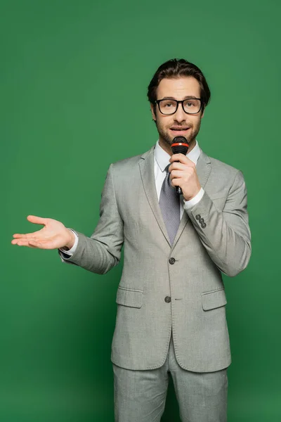 News anchor in suit talking at microphone and pointing with hand on green background — Stock Photo