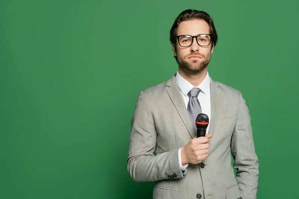 Ведущий новостей брюнеток в очках, держащий микрофон и смотрящий на камеру на зеленом фоне — стоковое фото