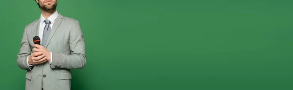 Vista ritagliata del newscaster in giacca che tiene il microfono su sfondo verde con spazio di copia, banner — Foto stock