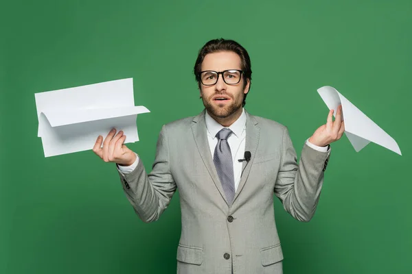 Confused news anchor in eyeglasses and suit holding blank papers on green — Stock Photo