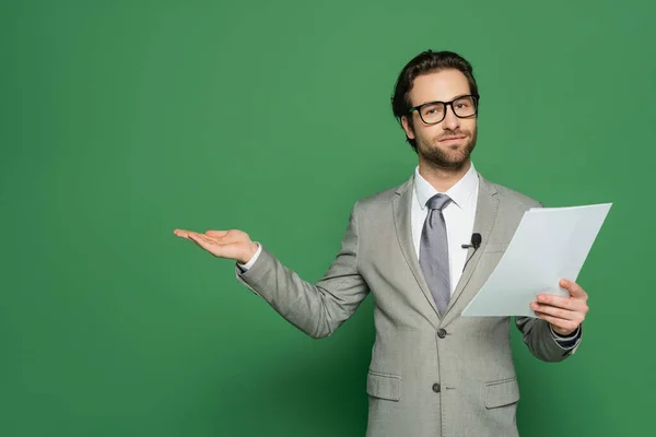 Nachrichtenanker in Brille und Anzug hält leeres Papier und zeigt mit der Hand auf grün — Stockfoto