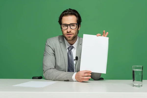 Bärtiger Nachrichtensprecher in Brille und Anzug, der leeres Papier auf Grün isoliert hält — Stockfoto