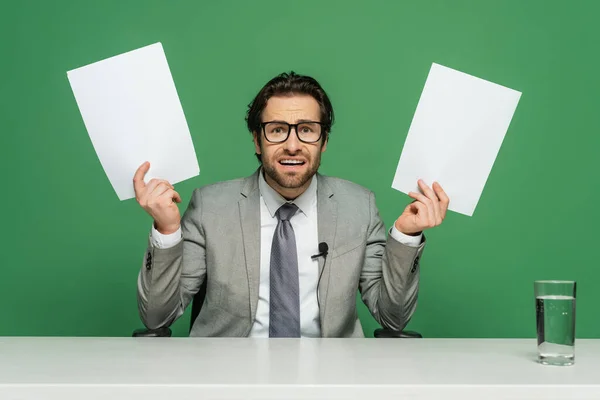 Anclaje de noticias emocionales en anteojos y traje con papeles en blanco aislados en verde - foto de stock