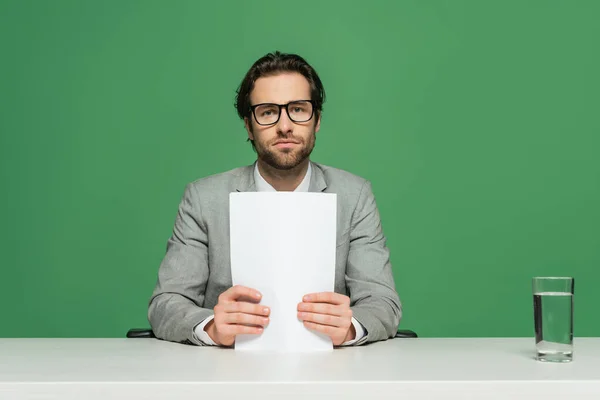 Young broadcaster in eyeglasses and suit holding blank paper isolated on green — Stock Photo