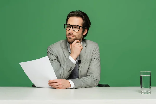 Pensativo locutor en gafas y traje sosteniendo papel en blanco aislado en verde - foto de stock