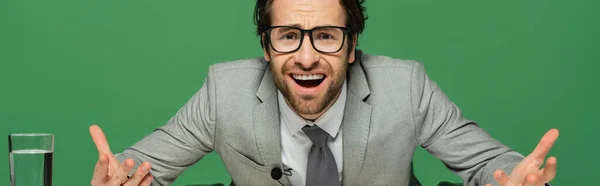 Emotional news anchor in eyeglasses and suit gesturing isolated on green, banner — Stock Photo