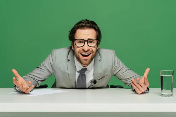 Emotional news anchor in eyeglasses and suit gesturing isolated on green — Stock Photo