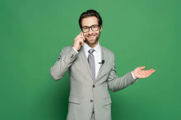 Reportero sonriente en gafas y traje hablando en el teléfono inteligente sobre fondo verde - foto de stock