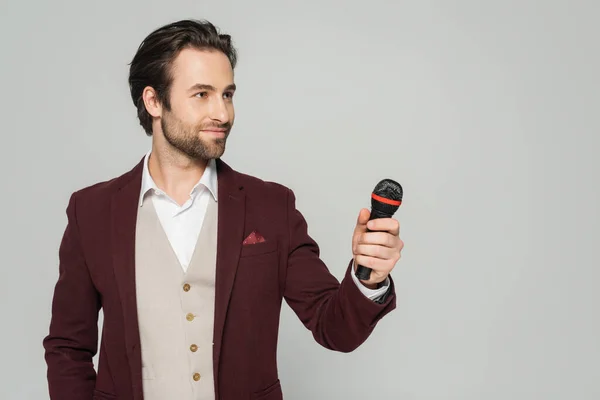 Moderatorin im roten Blazer hält Mikrofon isoliert auf grau — Stockfoto