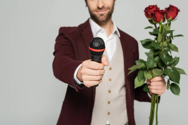 Vue recadrée de l'hôte flou de l'événement dans le blazer rouge tenant des roses rouges et microphone isolé sur gris — Photo de stock