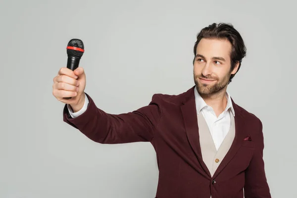 Cheerful host of event in formal wear looking at microphone isolated on grey — Stock Photo