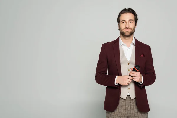 Young host of event in formal wear looking at camera while holding microphone isolated on grey — Stock Photo