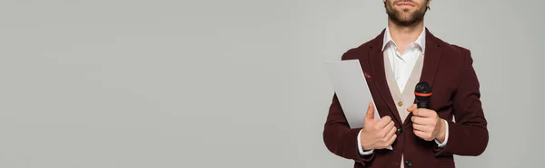 Cropped view of bearded host of event in formal wear holding microphone and clipboard isolated on grey, banner — Stock Photo