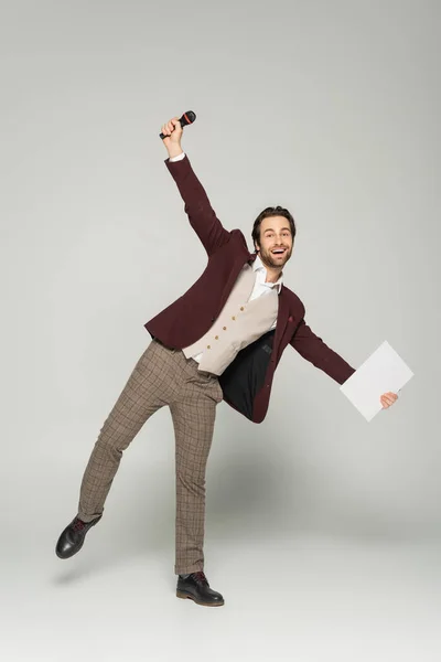 Full length of excited host of event in formal wear holding microphone on grey — Stock Photo