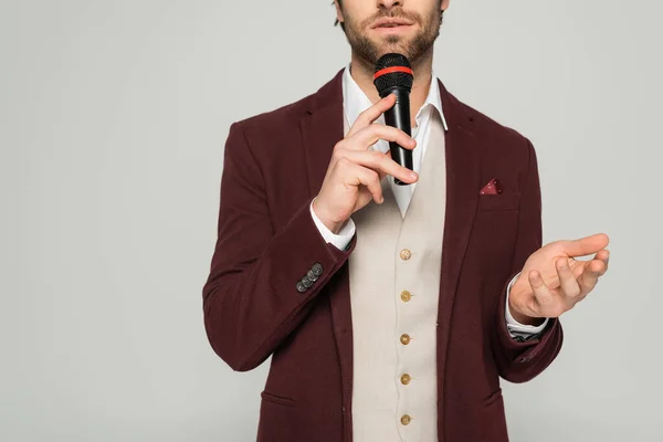 Ausgeschnittene Ansicht eines bärtigen Moderators in formeller Kleidung, der ein Mikrofon in der Hand hält und isoliert auf grau spricht — Stockfoto