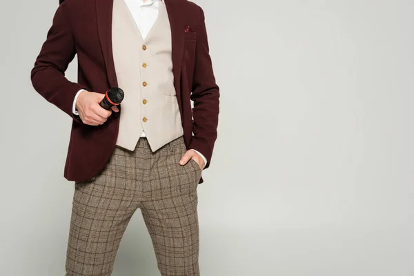 Обрезанный вид шоумен в формальной одежде стоя с рукой в кармане и держа микрофон изолирован на сером — стоковое фото
