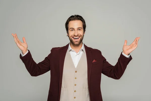 Amazed showman in red blazer gesturing while looking at camera isolated on grey — Stock Photo