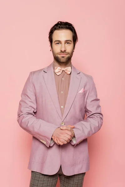 Bearded and young showman in suit with bow tie standing with clenched hands isolated on pink — Stock Photo