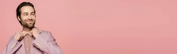 Positive and young showman in suit adjusting bow tie isolated on pink, banner — Stock Photo
