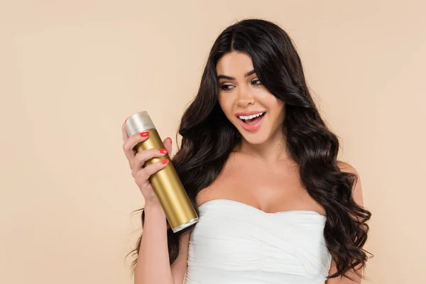 Excited woman with wavy hairstyle holding hairspray isolated on beige — Photo de stock