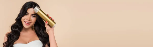 Smiling brunette woman holding hairspray isolated on beige with copy space, banner — Photo de stock