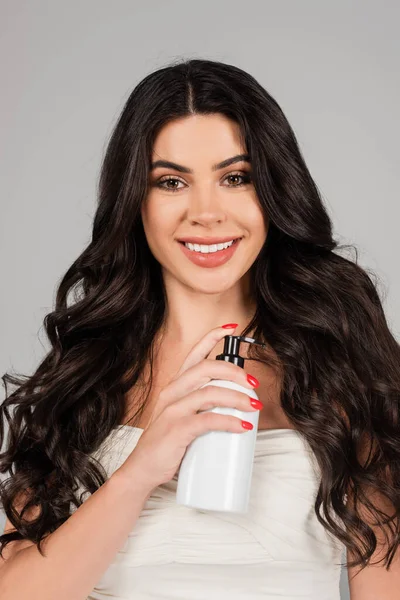 Happy and brunette woman holding bottle with hair product isolated on grey — Stock Photo